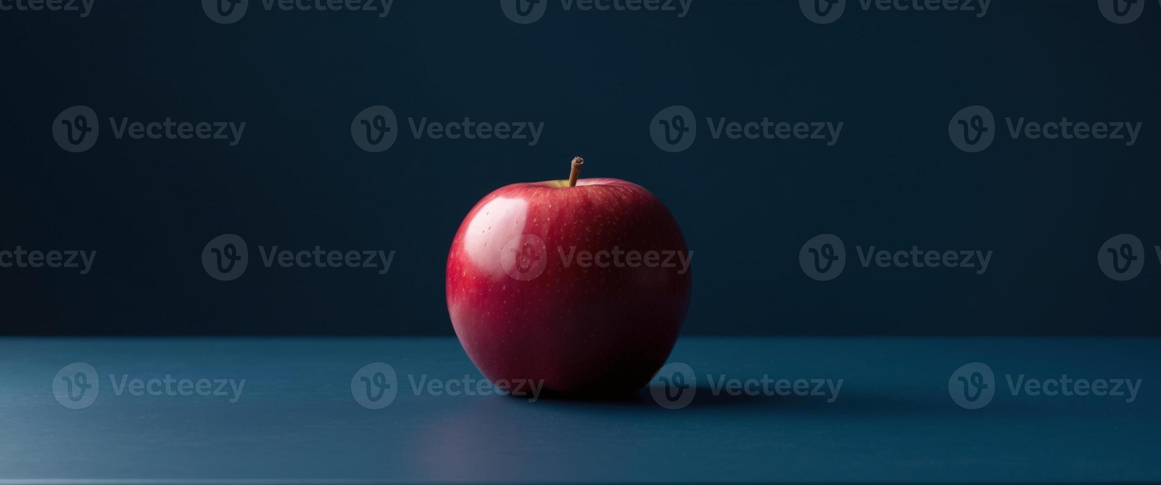 A single ripe red apple resting on a dark blue table. photo