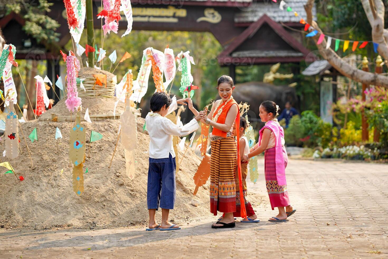Group of Thai children's with beautiful Thai young woman in the Thai traditional dress playing human cave train on outdoor pile of sand in temple at the Songkran festival. photo
