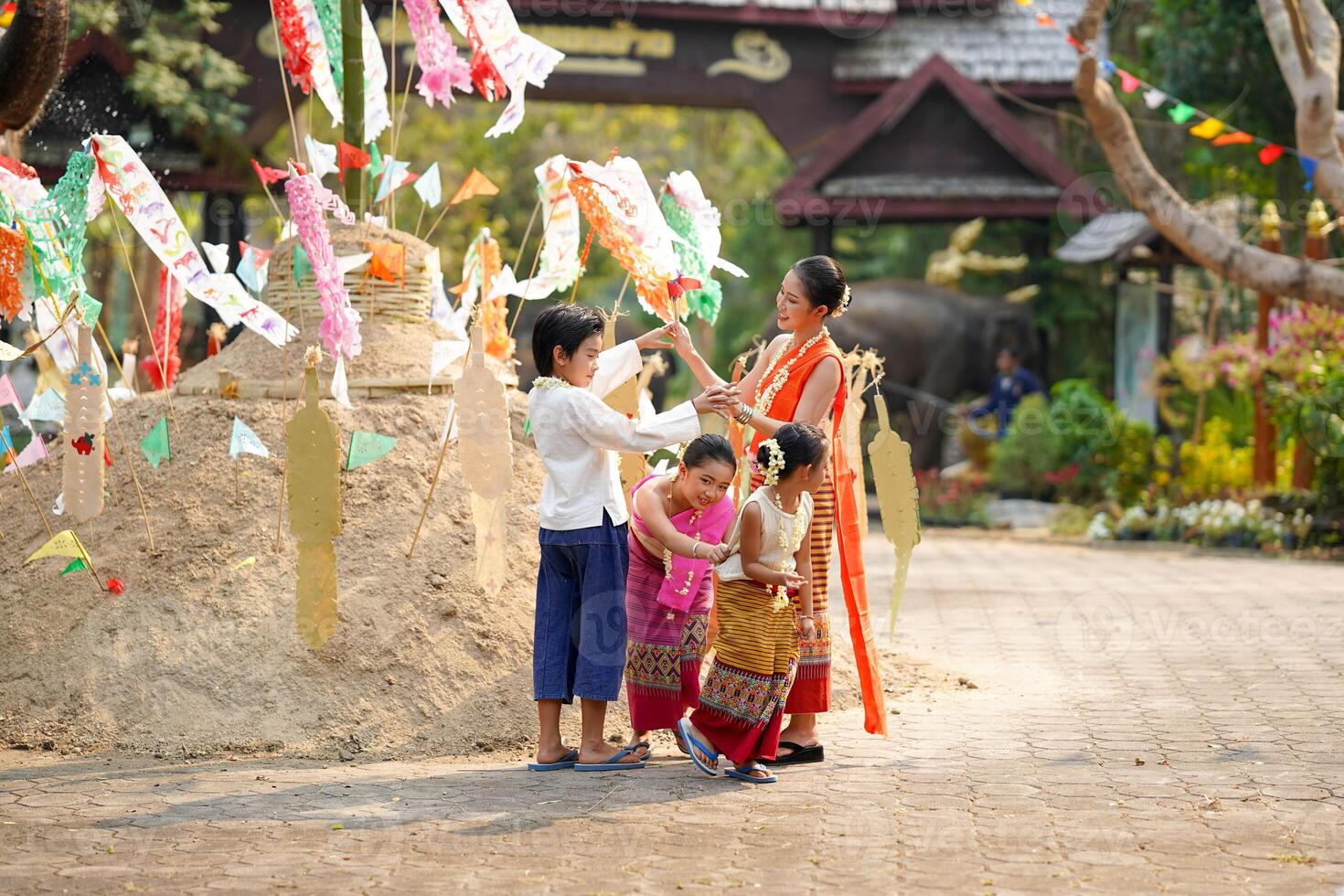 Group of Thai children's with beautiful Thai young woman and in the Thai traditional dress playing human cave train on outdoor pile of sand photo