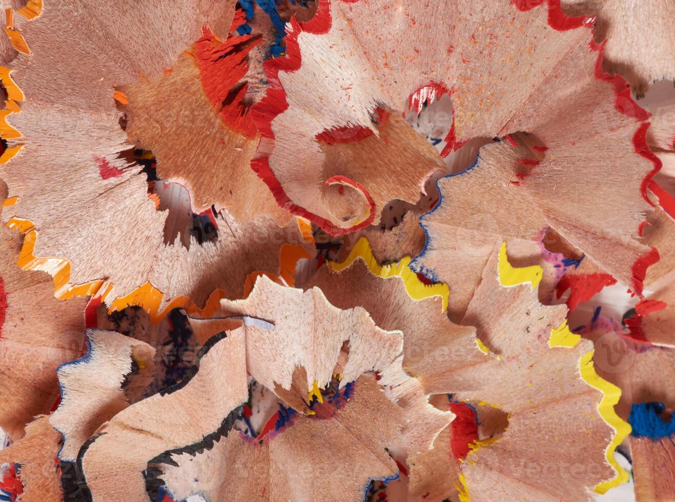 Colorful pencil shavings in red, yellow, blue, and wood tone. The shavings are curled and layered photo