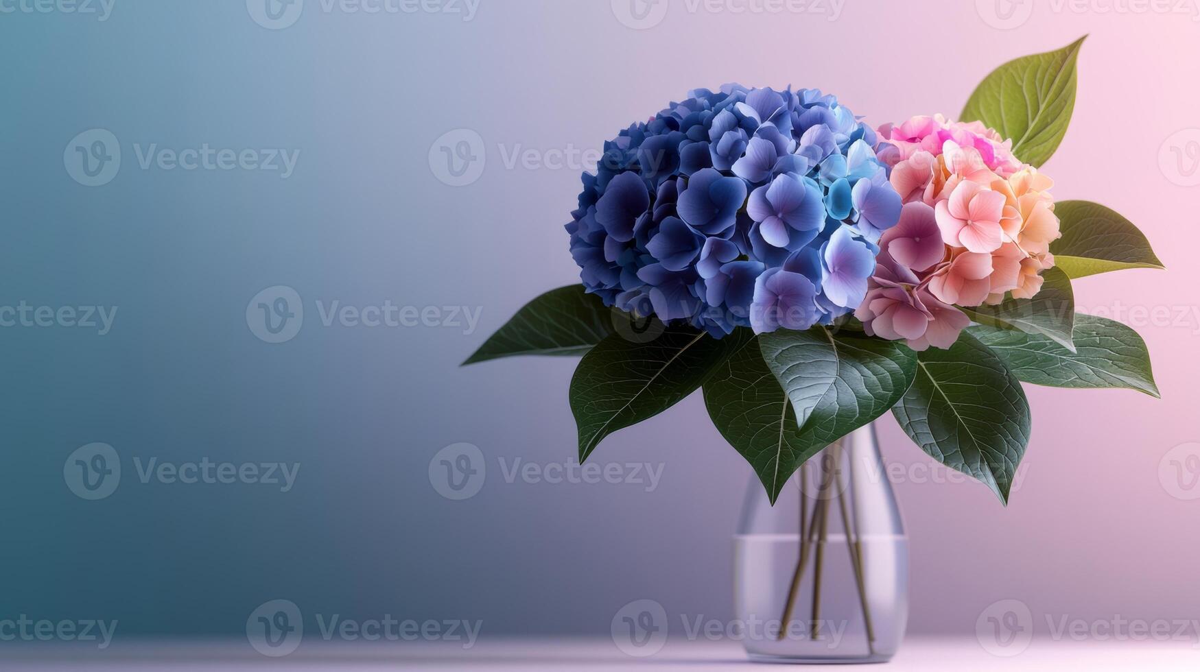 Vase of blue and pink flowers sits on a table. The flowers are in a clear vase and are surrounded by green leaves photo