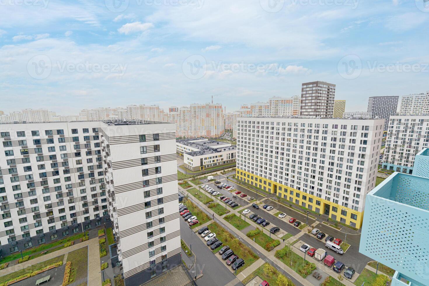 A city view with a lot of buildings and cars. The buildings are mostly white and the cars are parked in the parking lot. photo