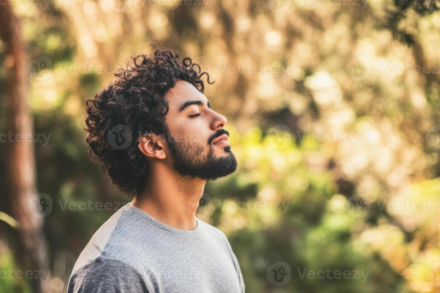A man with curly hair and a beard is standing in the woods photo