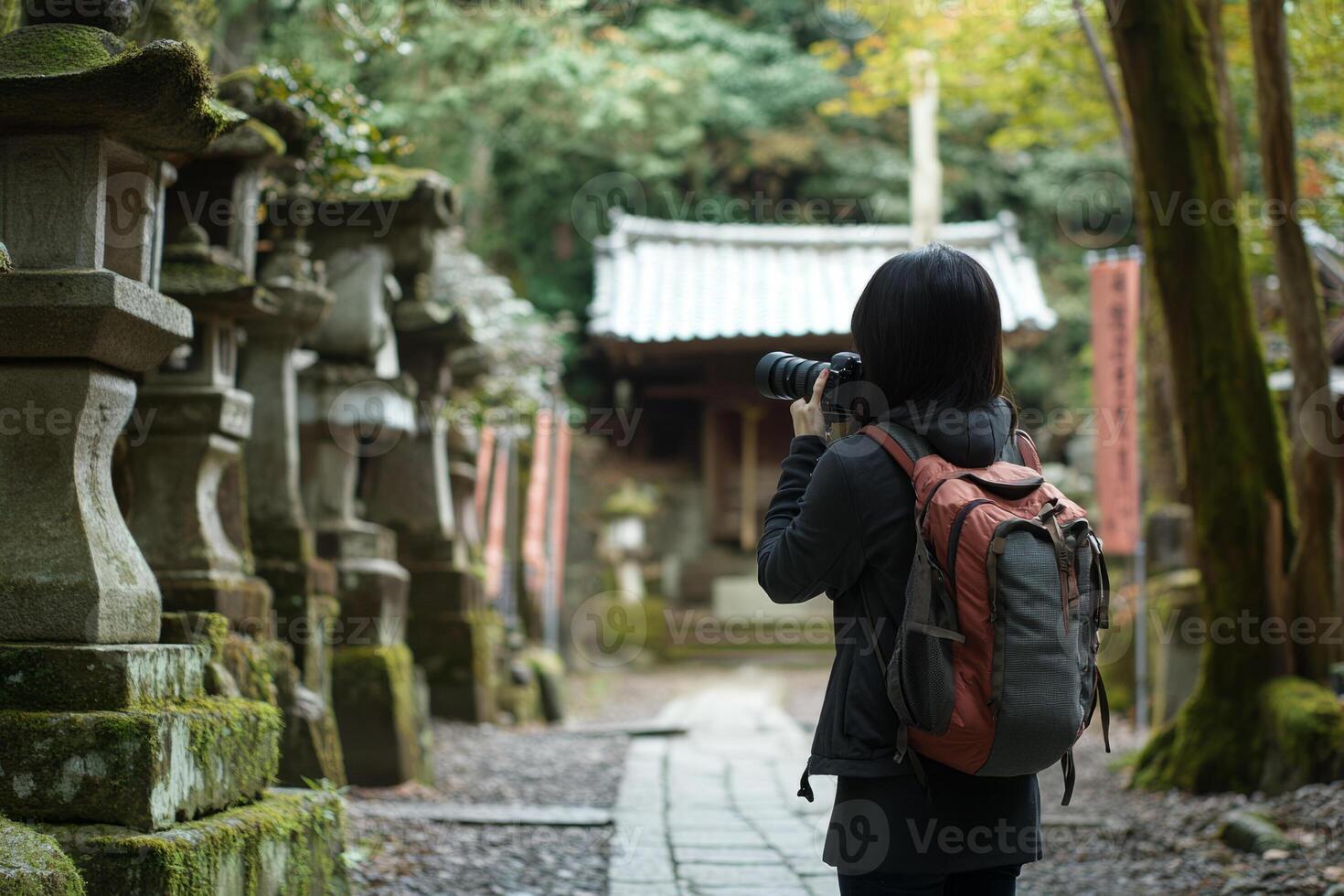 A woman with a backpack taking a photo of a stone wall