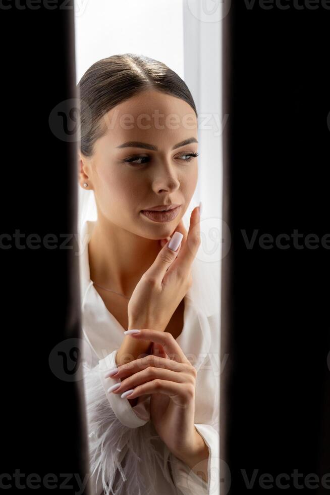 Bride hiding behind curtains looking down with closed eyes and hands near her face. photo