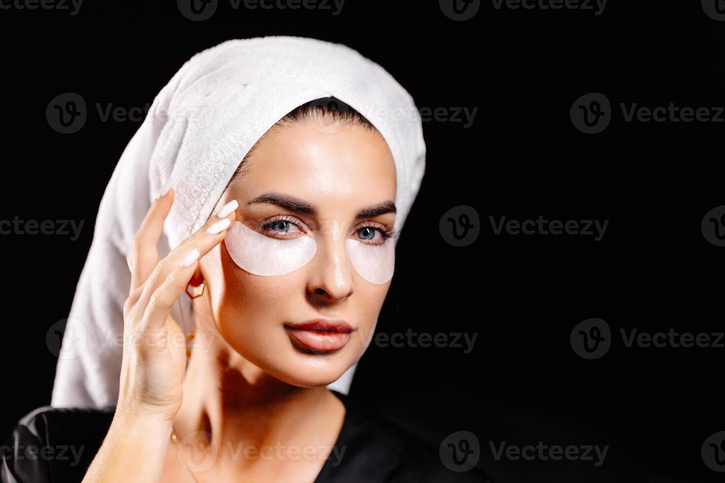 Young woman in white towel and robe taking on eye patch looking in camera photo