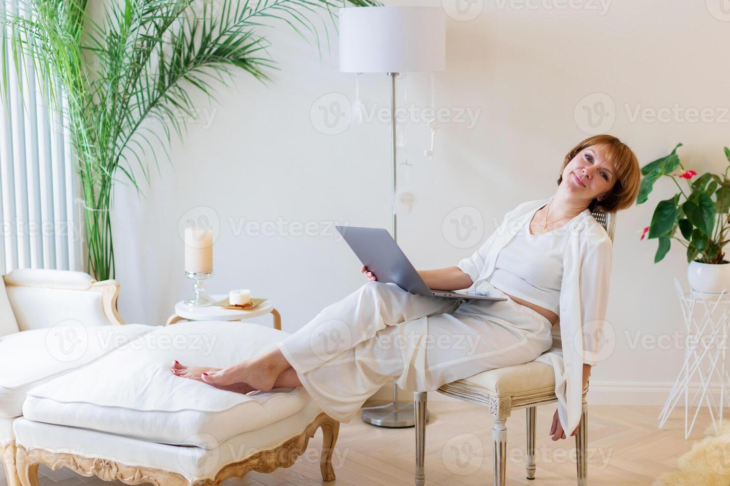 Senior stylish woman sitting with her laptop and making a pause in working day at home. Adult freelancer is tired and make a pause while working on laptop in living room. photo