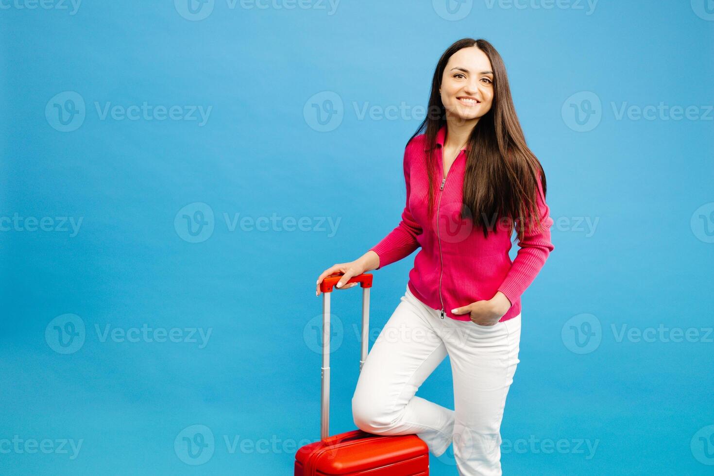 Traveler woman holding a suitcase handle, standing isolated on blue background studio photo