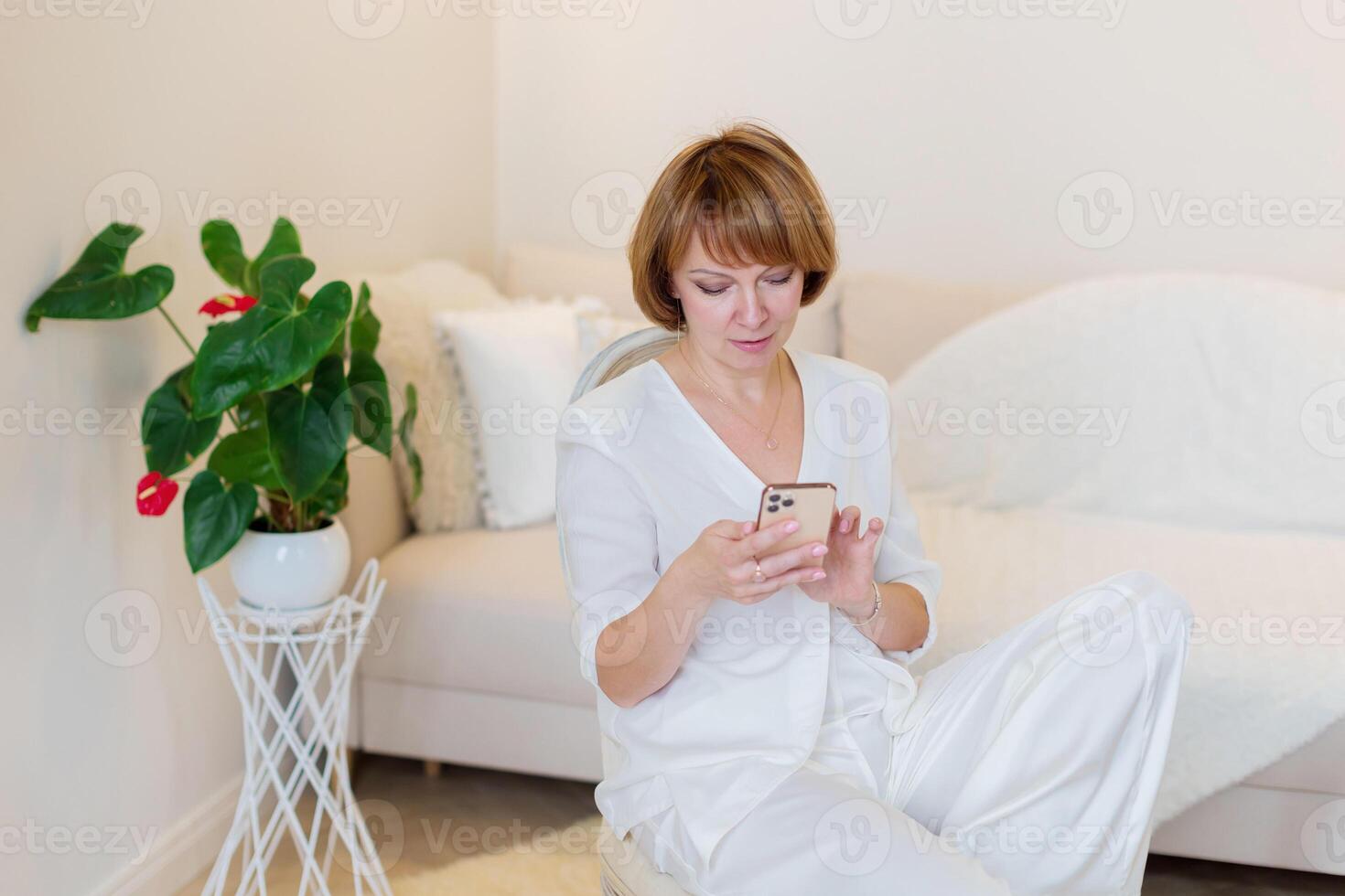 Adult beautiful woman relax siting on chair at home and using cellphone texting chatting with friend. Happy young woman on chair holding smartphone in her hands, shoping online or check social media. photo