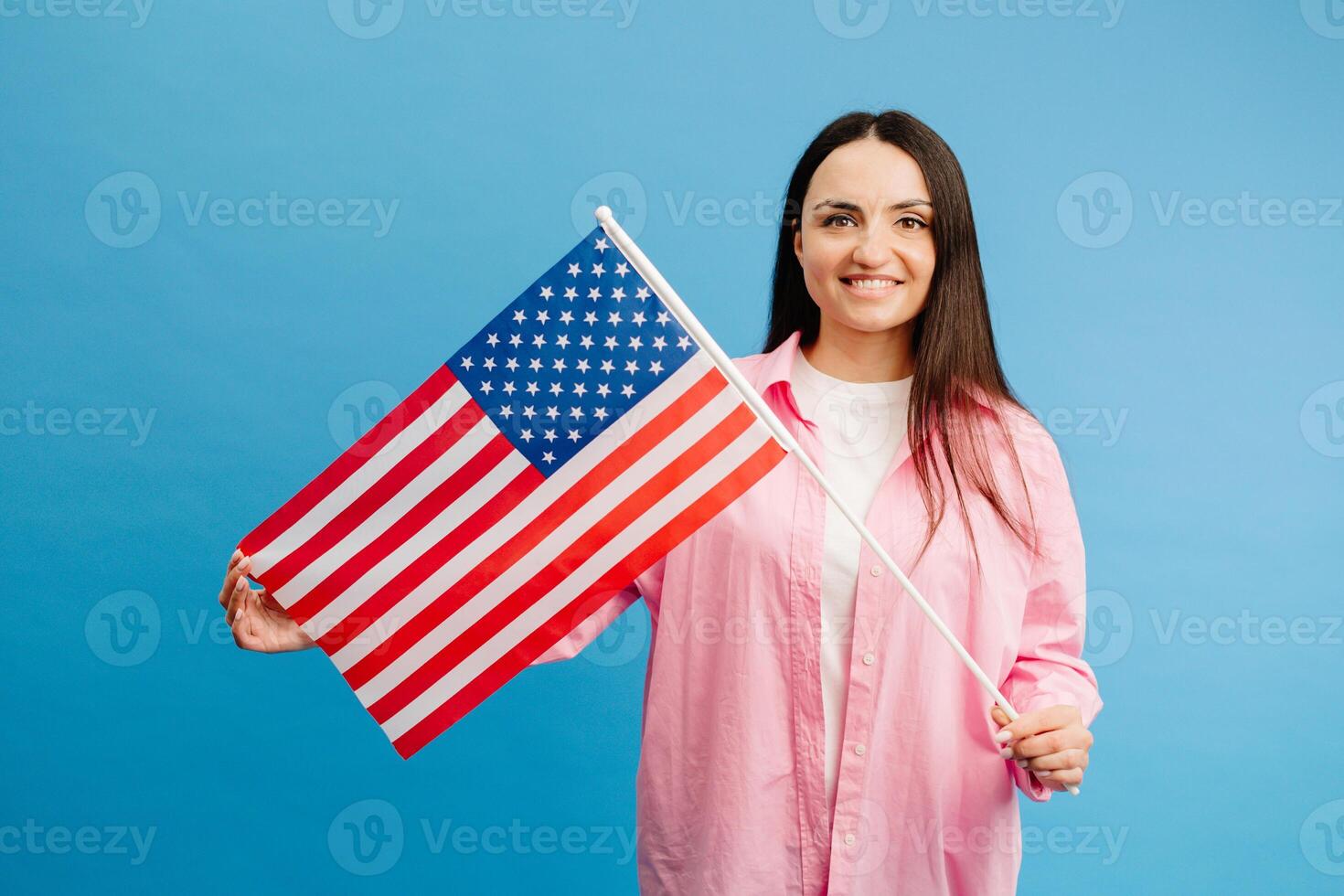 Young smiling happy woman wears casual clothes holding american flag and looking to the camera isolated on blue color background. photo