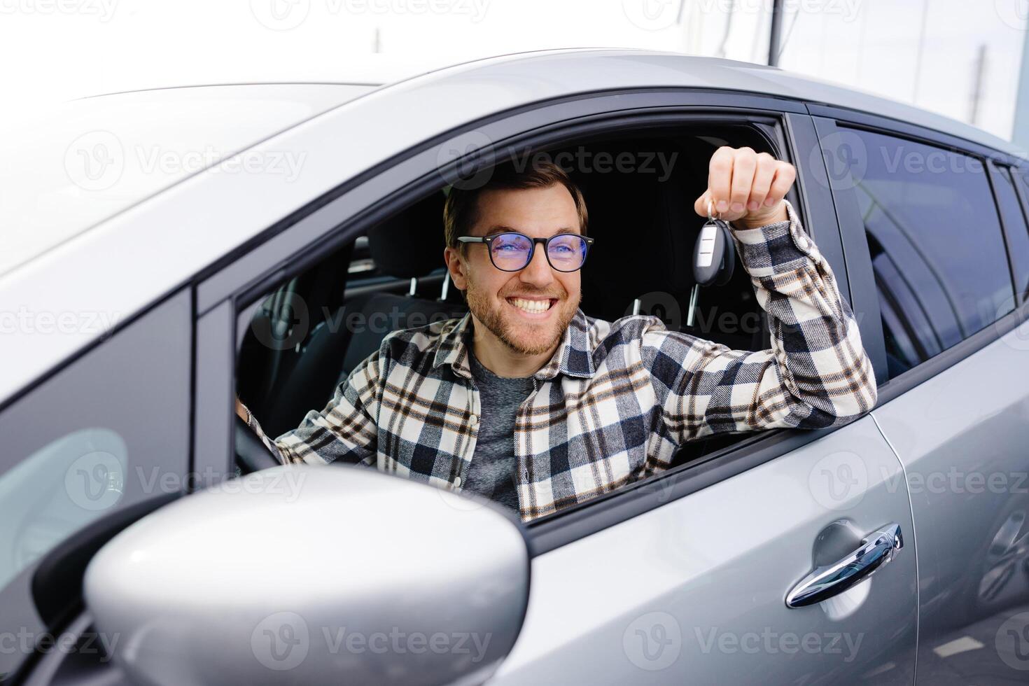 Excited man showing a car key, sitting inside new vehicle. photo