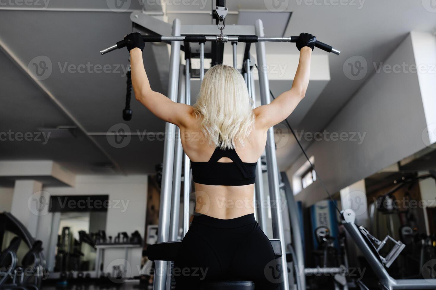 Athletic woman exercising back muscles using lat machine in gym photo
