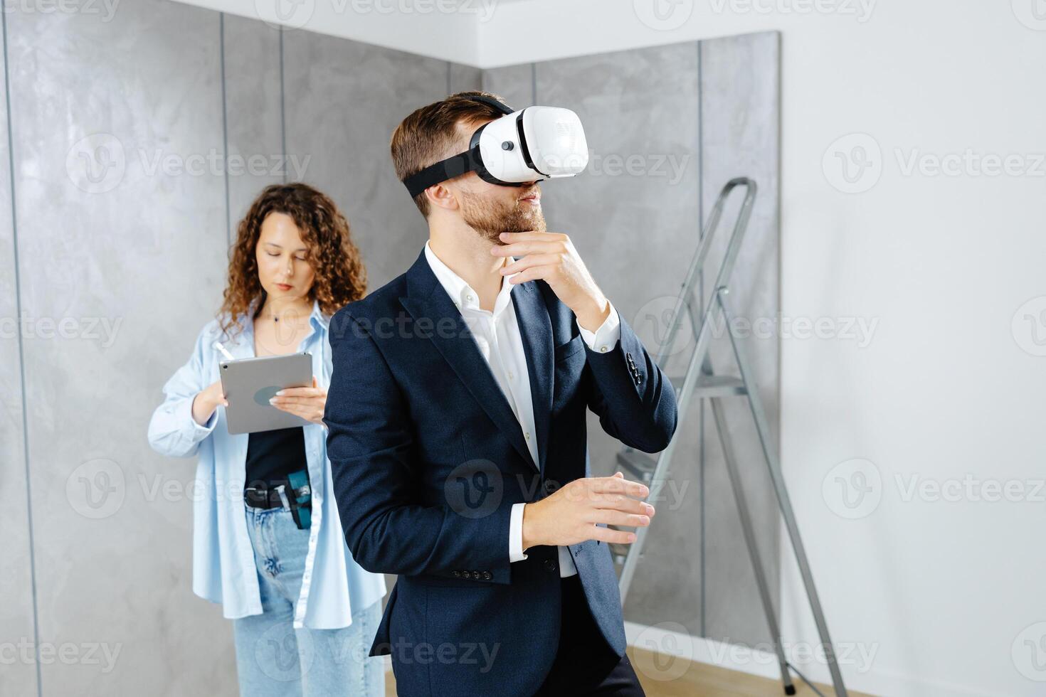 Man client wearing VR glasses imagining future interior standing with designer at the construction site photo