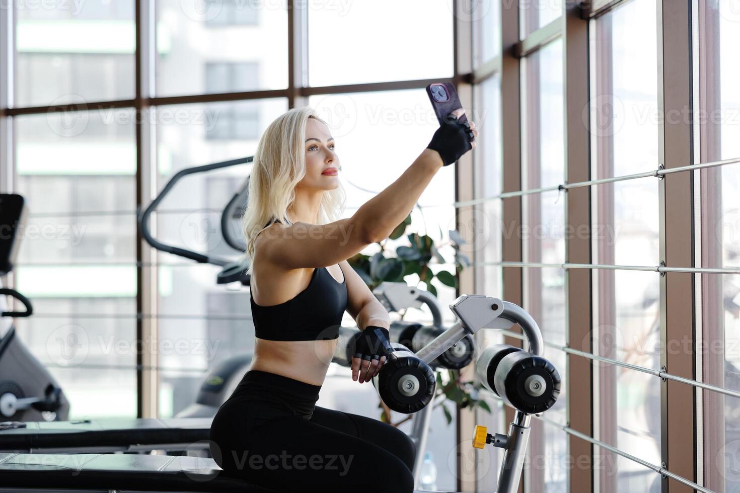 Athletic woman resting on bench after exercising with dumbbells in gym photo