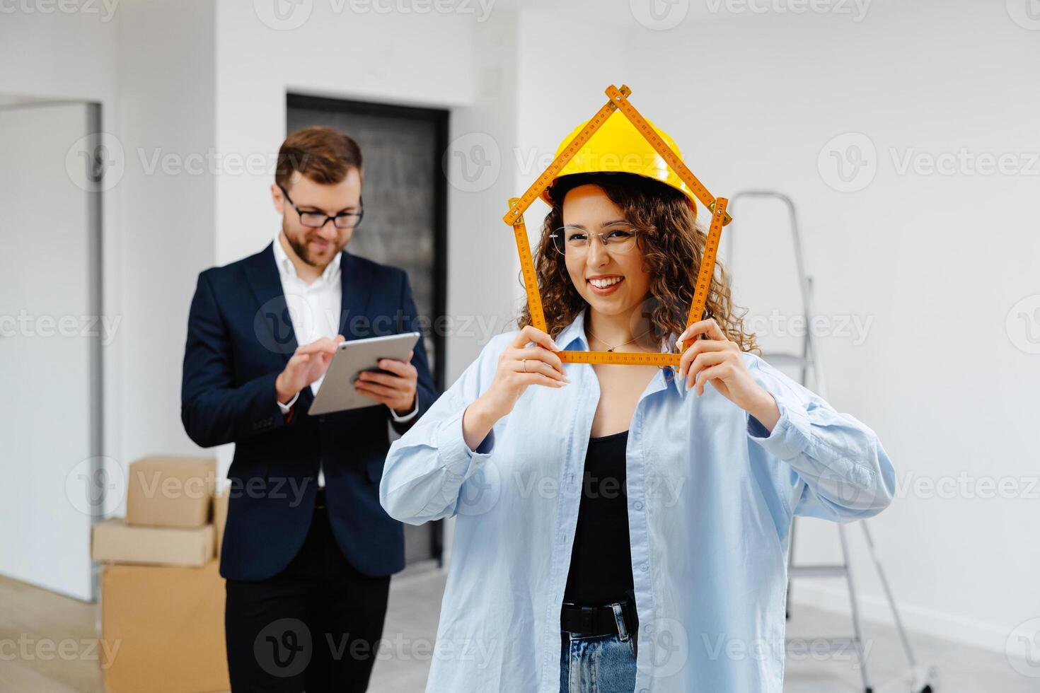 Young businessman is holding a tablet and looking at the modeling of an apartment, while a designer is standing with a ruler in her hands and looking at the camera. photo