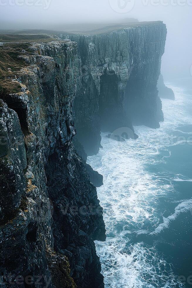 Dramatic coastal cliffs meet turbulent ocean waves in misty weather photo