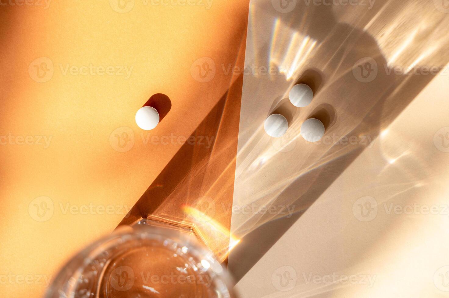 white medical pills lie on the background, next to a transparent glass of water. A shadow from a glass of water falls on an orange background. pills are white, round. top view. medical concept photo