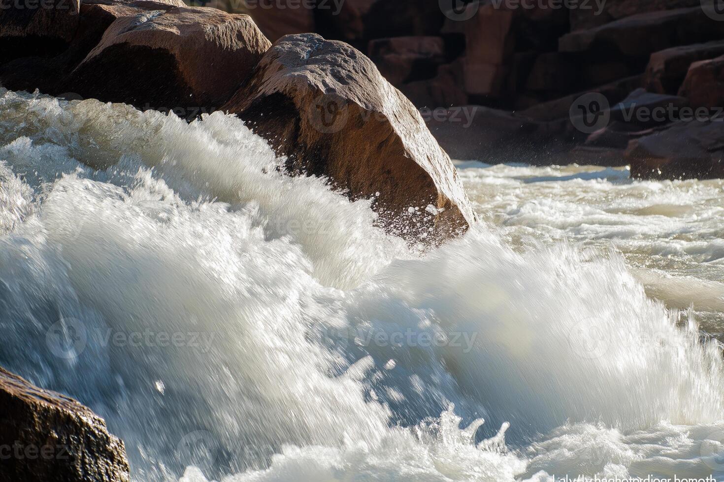 Whitewater shows turbulent journey rushing past large river boulder photo