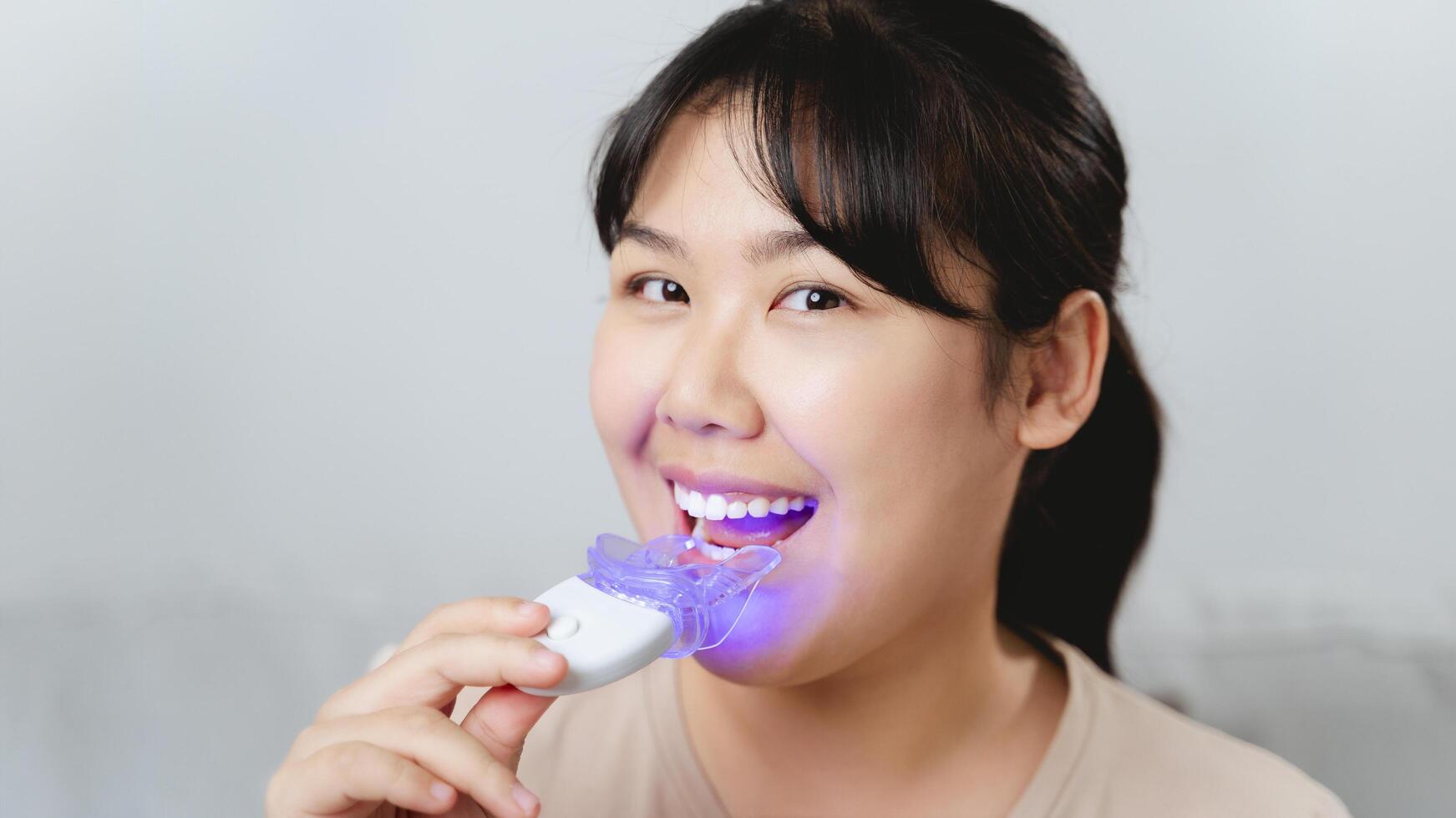 The woman is bleaching her teeth by herself using a whitening tool. photo