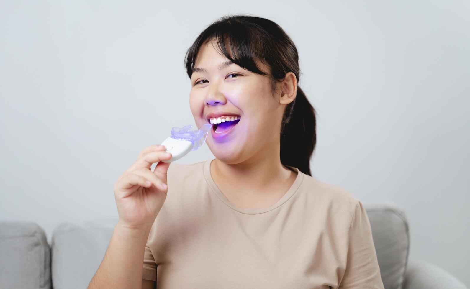woman is whitening her teeth with a teeth whitening device by herself photo