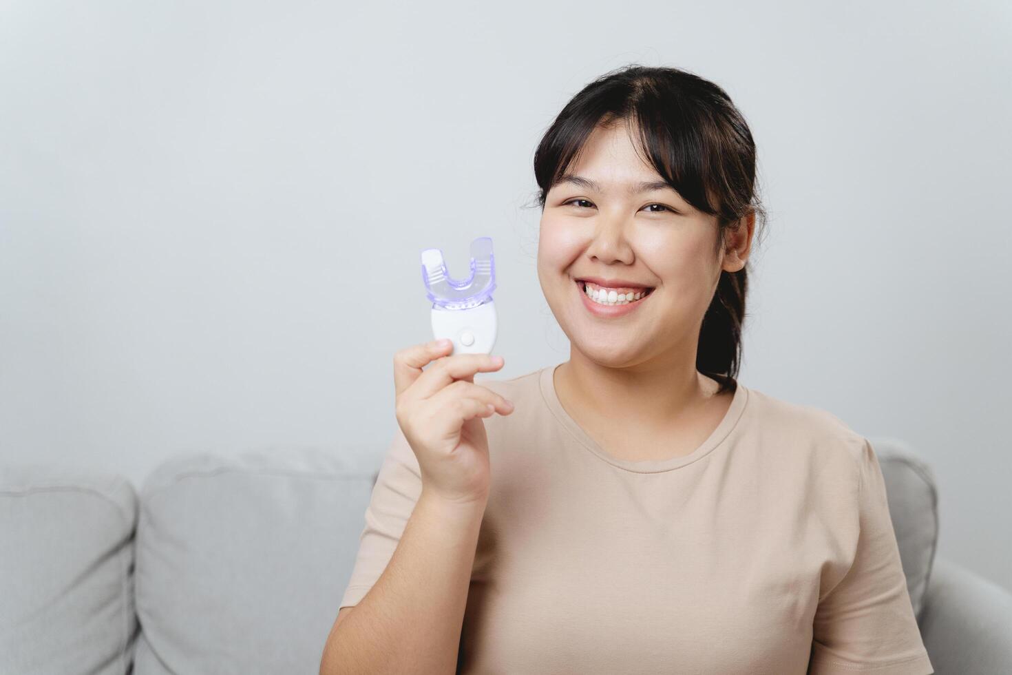 The woman she is using a teeth whitening device to whiten her teeth on her own. photo
