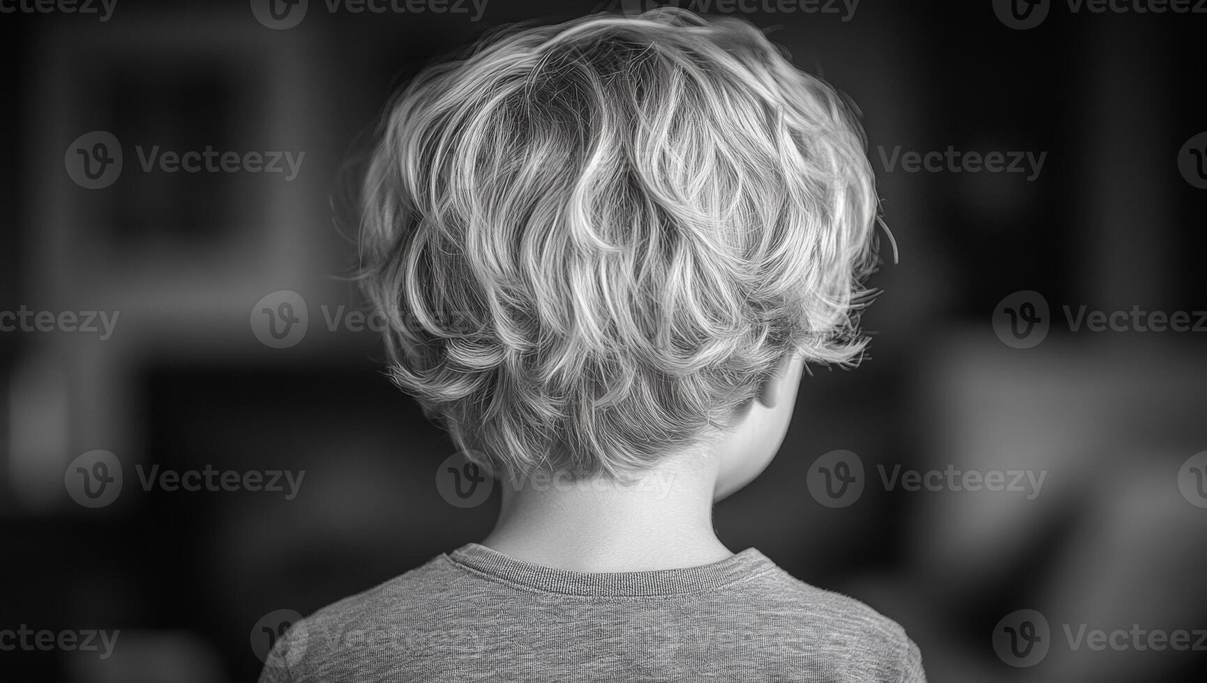 Curly-haired child in blur. A young child with light, curly hair stands with their back turned, surrounded by a softly blurred indoor setting. photo