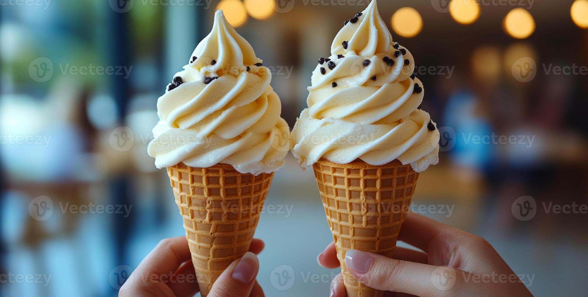 Enjoying ice cream cones on a sunny day. Two hands hold waffle cones filled with swirled soft serve ice cream topped with chocolate sprinkles. photo
