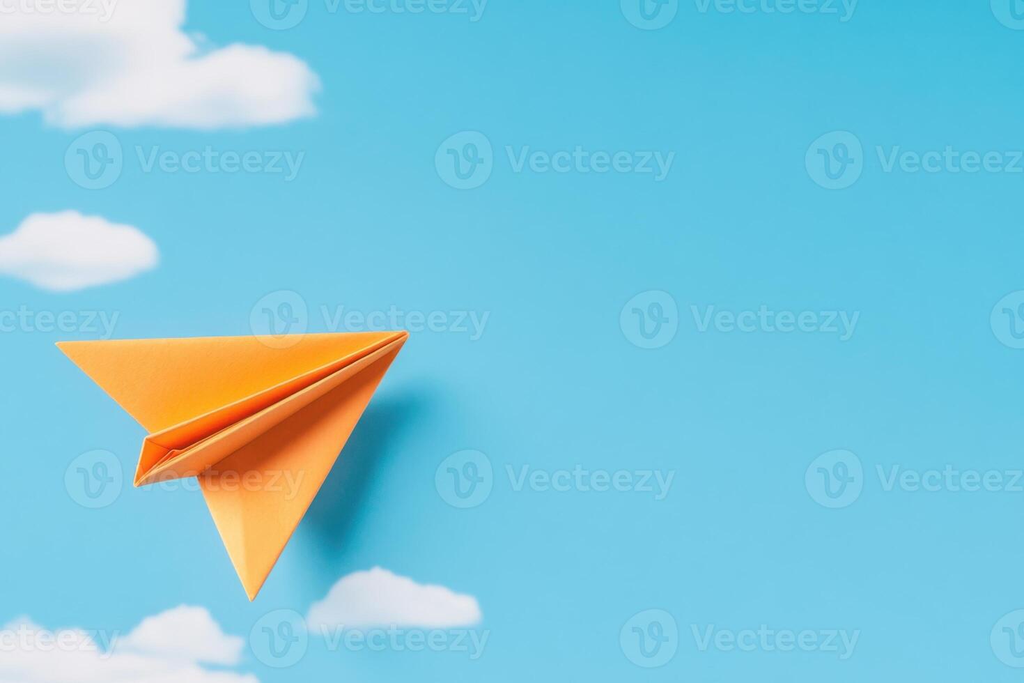 Orange paper airplane flying through a blue sky with clouds photo