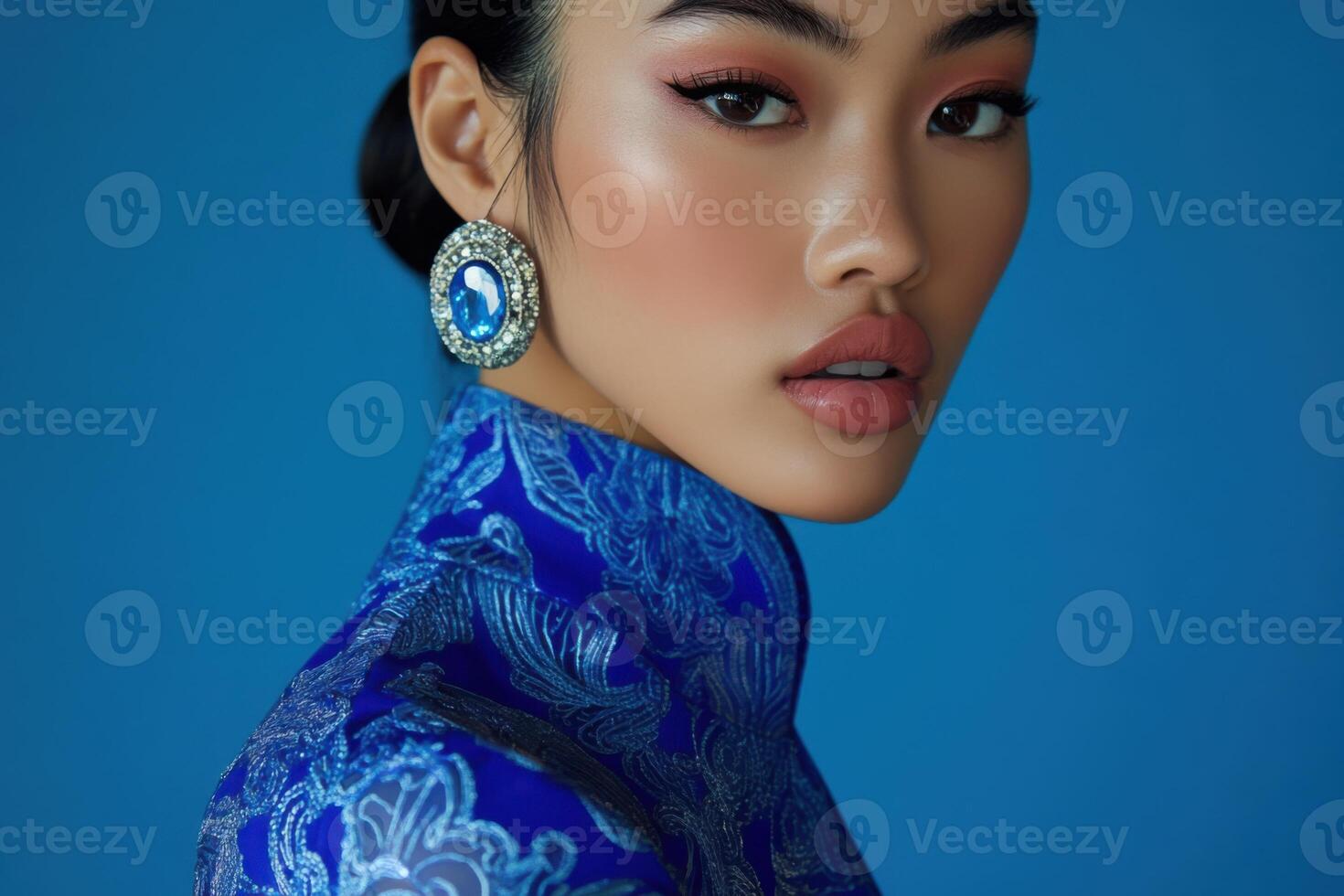 Fashion model wearing blue dress and earrings posing in studio photo
