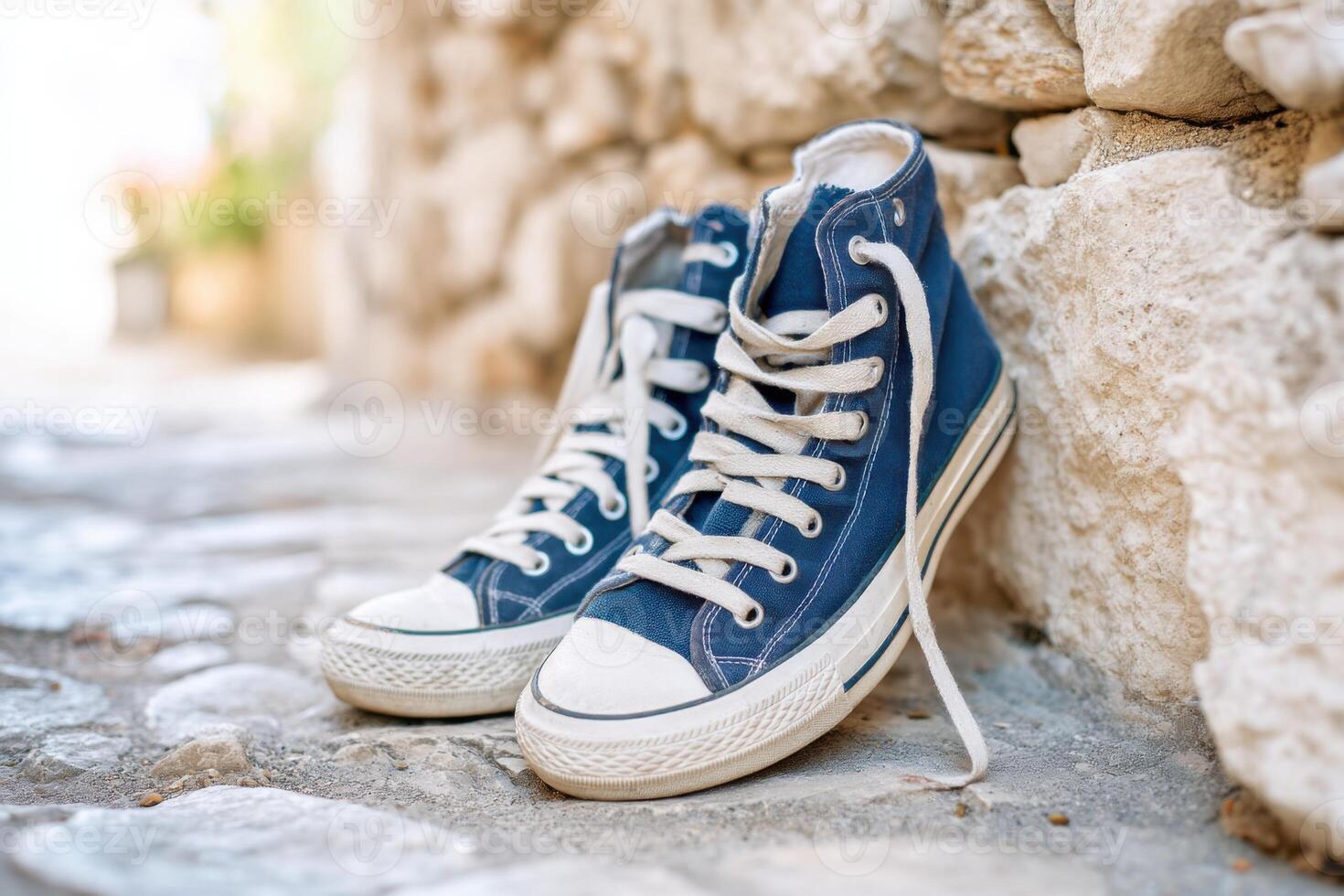 Worn blue sneakers resting against a stone wall in a cobblestone alley photo