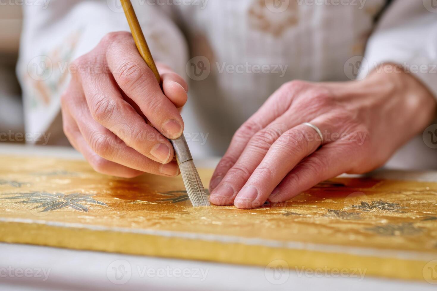 Master artisan painting intricate gold leaf details on wooden panel in traditional workshop during morning hours photo