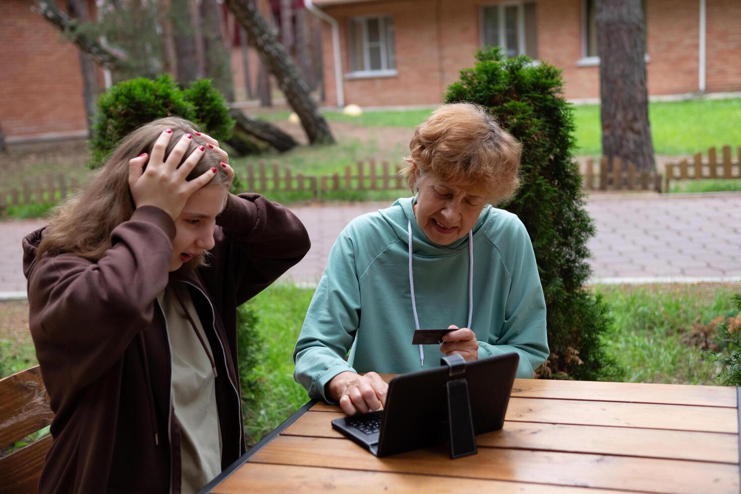 a happy teenage girl teaches older 70s grandmothers to use a laptop at home. social media and modern technologies a pensioner studies in online security. photo