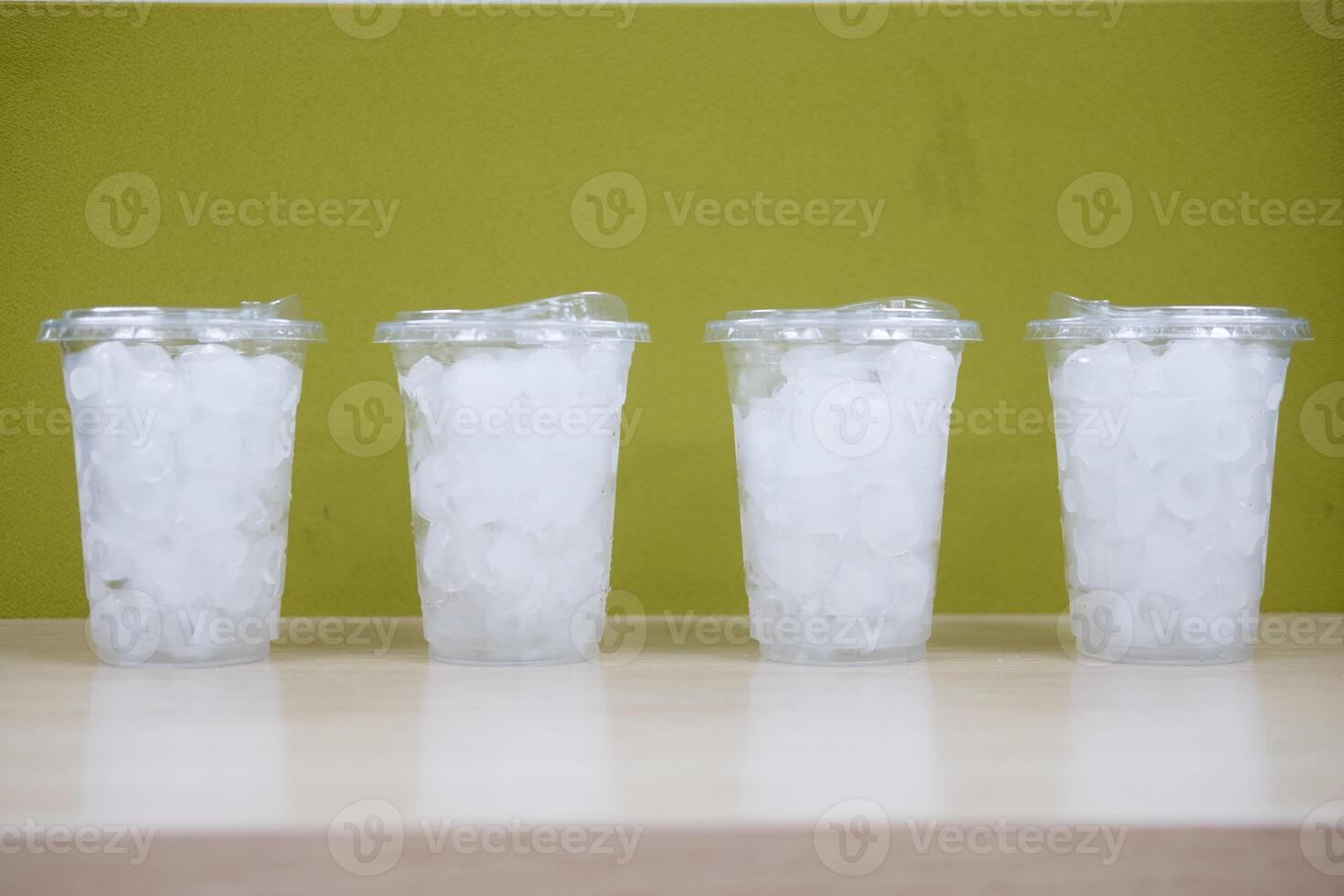 A row of four clear plastic cup with lid filled with ice cubes photo