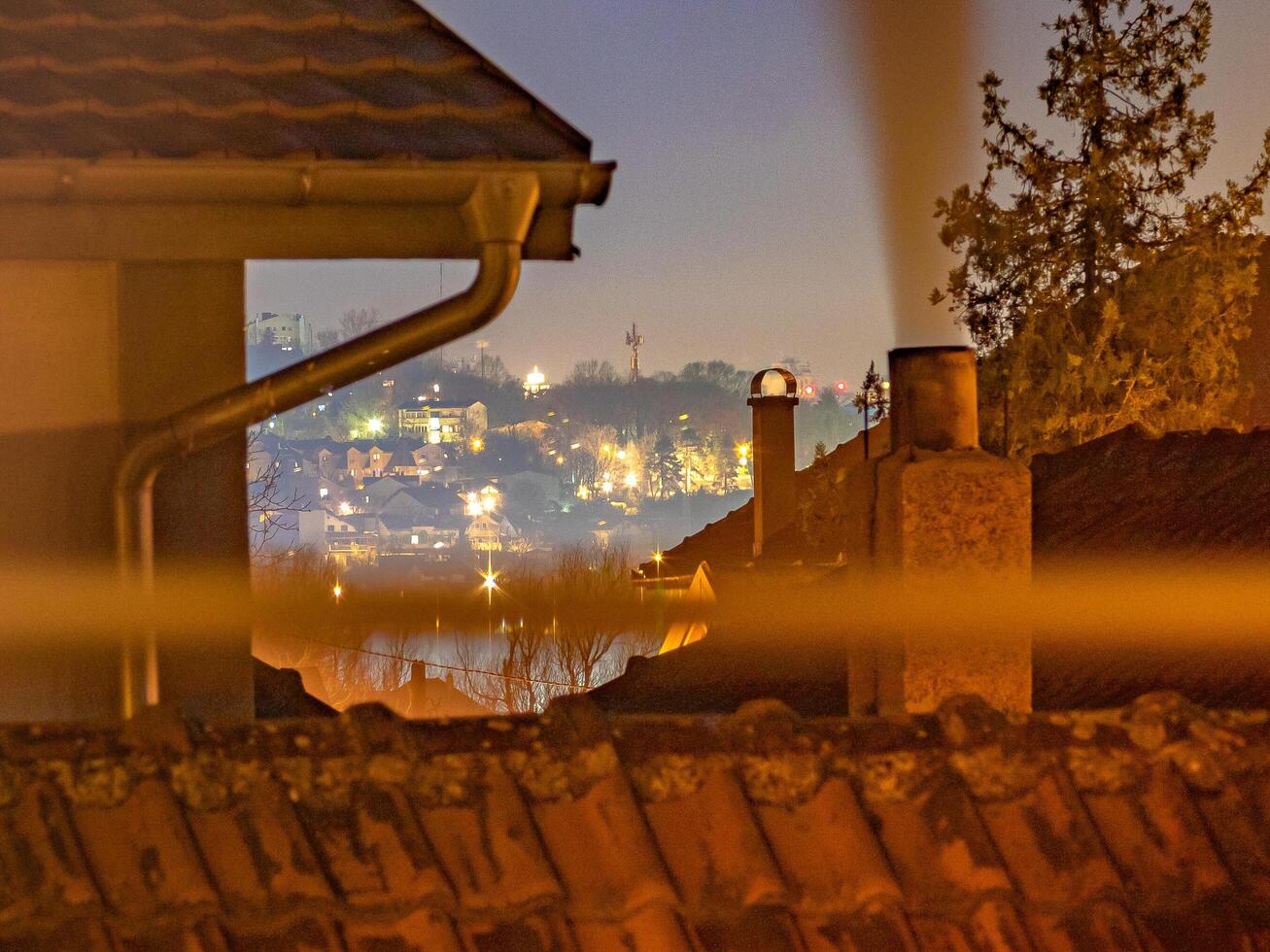 A warm-toned rooftop scene with chimneys and misty city lights, evoking nostalgia and urban serenity photo