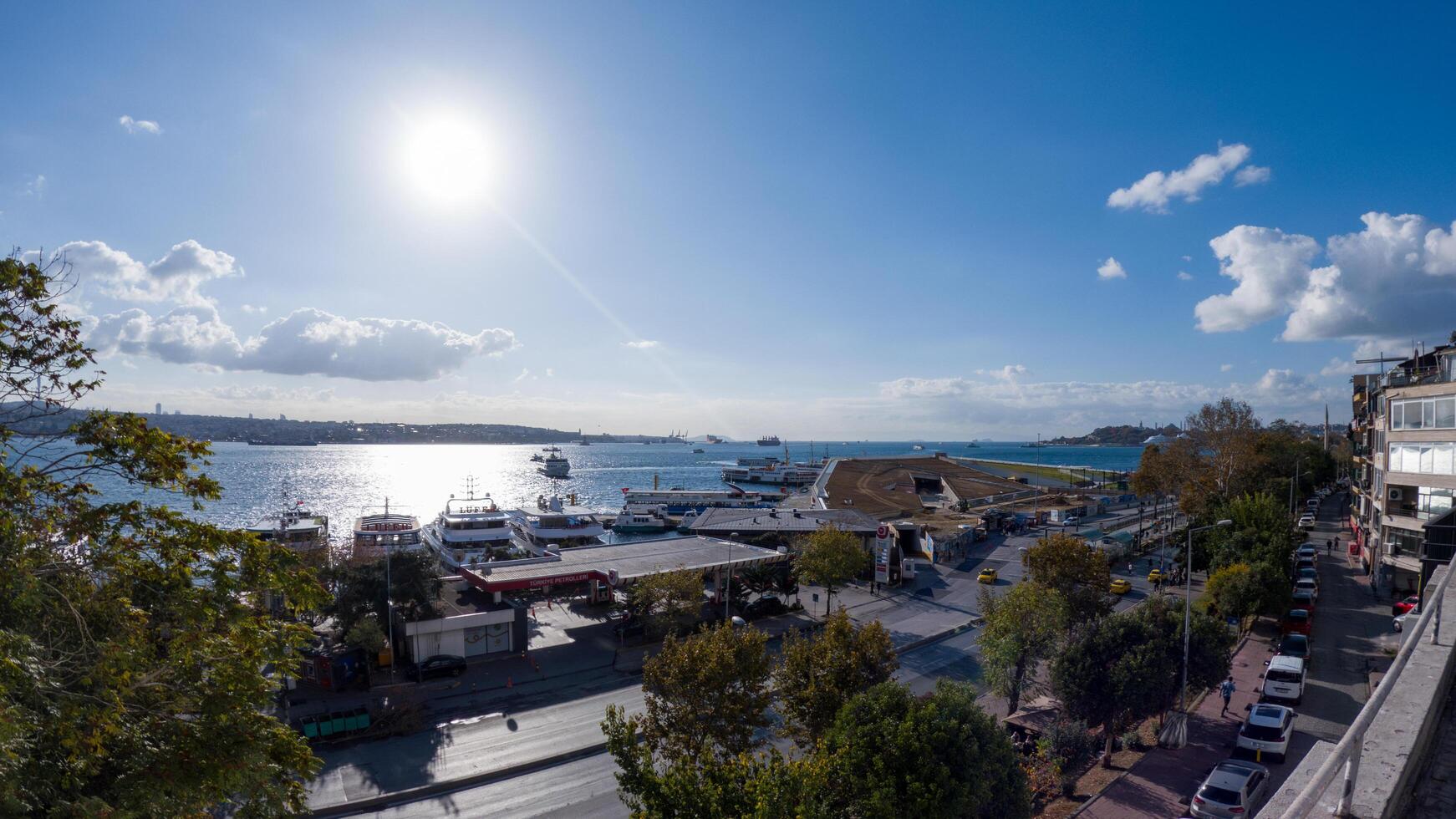 A breathtaking panoramic view of the Bosphorus Strait, featuring a vibrant harbor filled with boats and ferries. The sun shines brightly in the clear blue sky, casting a shimmering reflection. photo