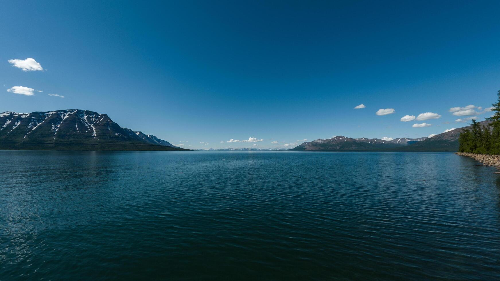 A vast, deep-blue lake stretches across the landscape, its rippling surface reflecting the crisp mountain air. Towering snow-capped peaks rise majestically in the distance. photo