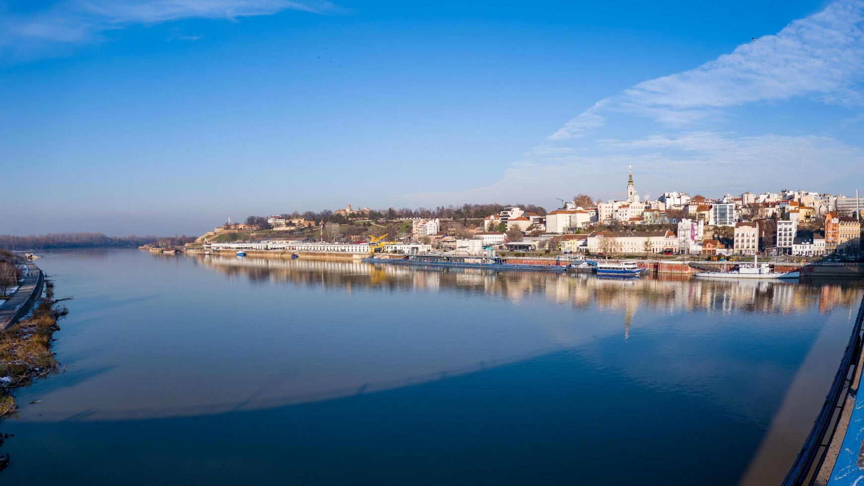 A stunning view of Belgrade, Serbia, showcasing the historic riverside, boats, and Kalemegdan Fortress under a clear blue sky, reflecting beautifully on the calm Danube River. photo