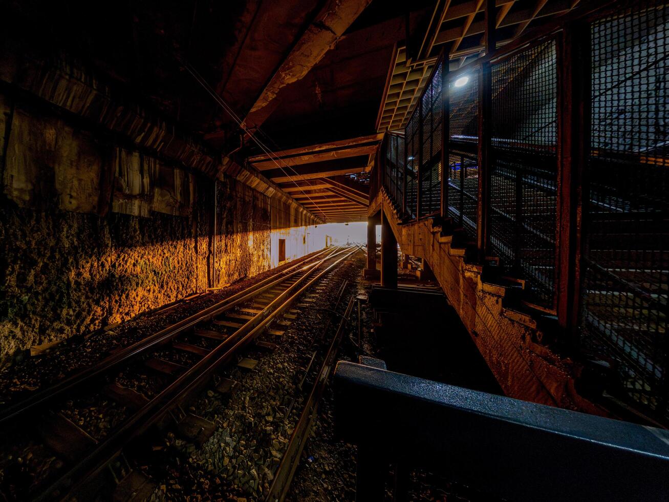 A dark underground railway tunnel illuminated by golden light at the exit, creating a striking contrast between shadow and brightness, evoking mystery and anticipation. photo