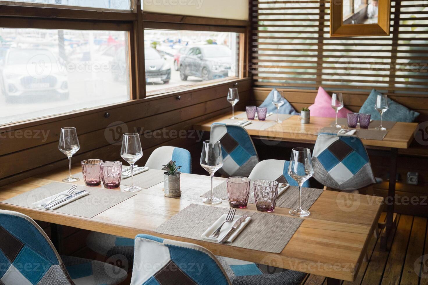 Cozy modern restaurant interior with wooden tables and geometric chairs by large windows photo