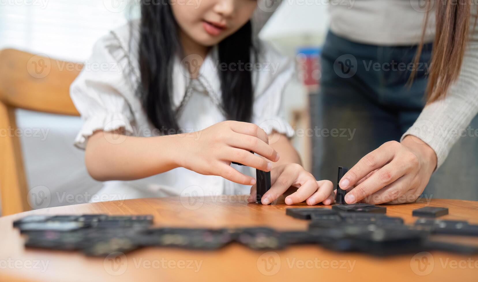 Creative Play and Cooperation. A mother assists her daughter as they build with dominoes together. photo