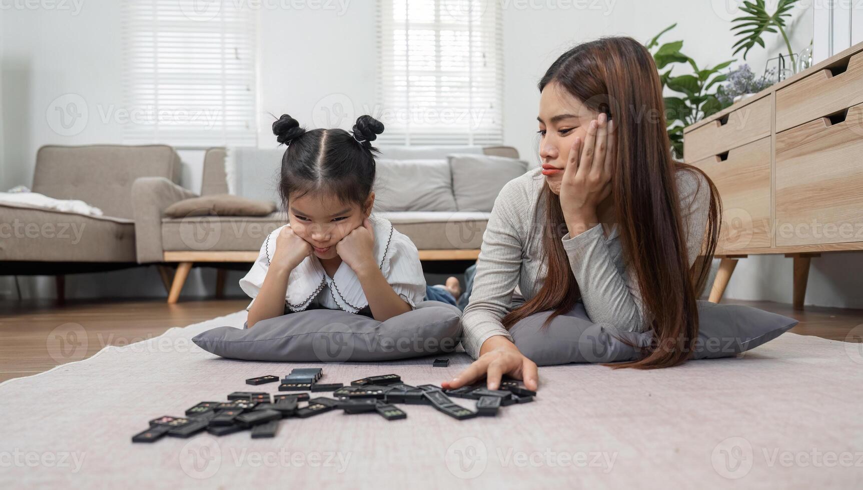 Family Moments and Emotional Connection. A mother and daughter share a thoughtful moment while playing with dominoes. photo