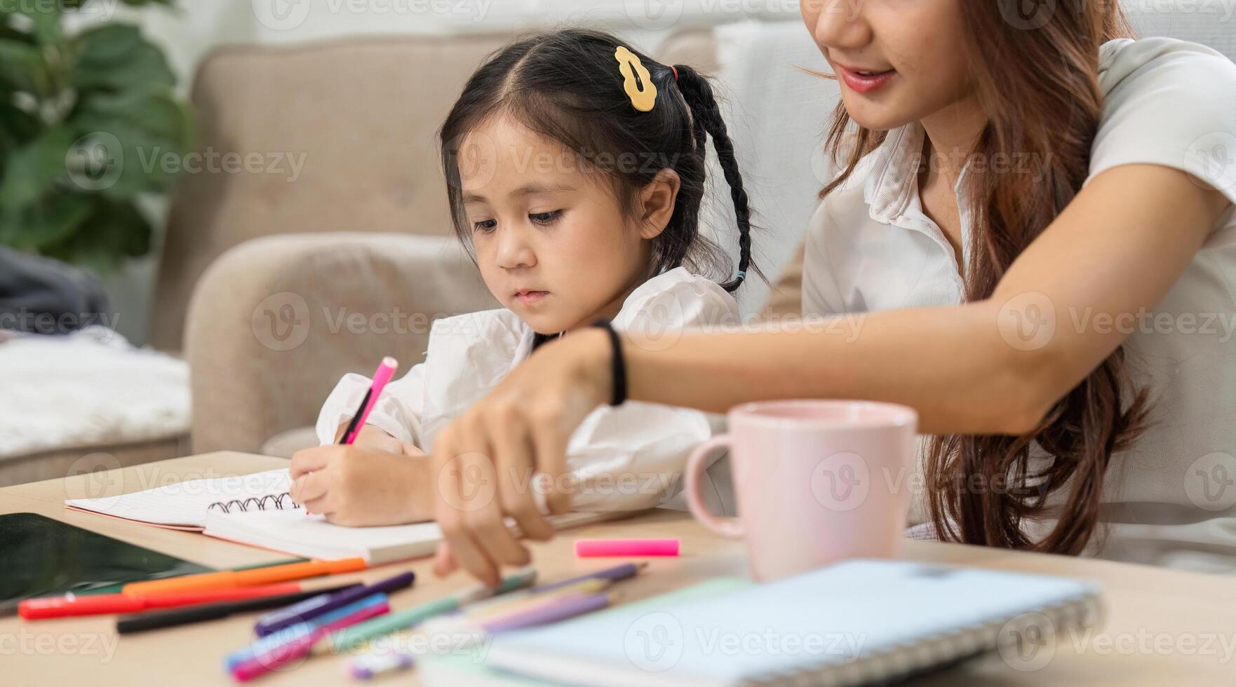 Creative Learning and Mother-Daughter Bonding. A mother helps her daughter with her homework at home with colorful stationery. photo
