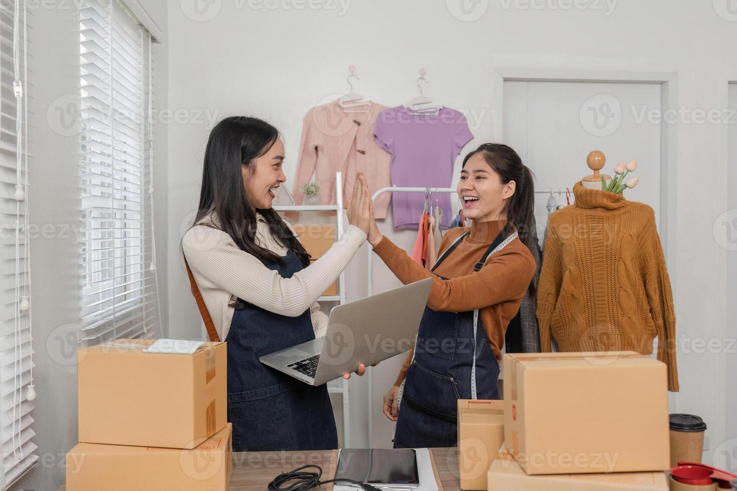 Joyful online sellers giving each other a high-five while reviewing orders on a laptop in their trendy boutique photo