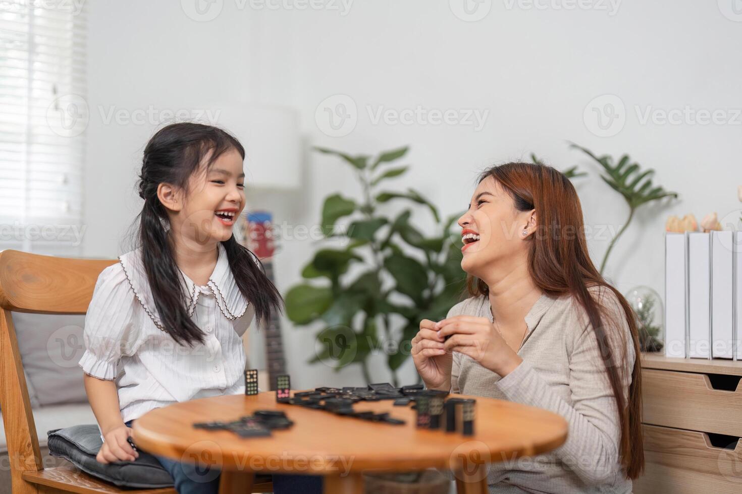 Family Fun and Bonding. A mother and daughter sharing laughter and joy while playing a domino game at home. photo
