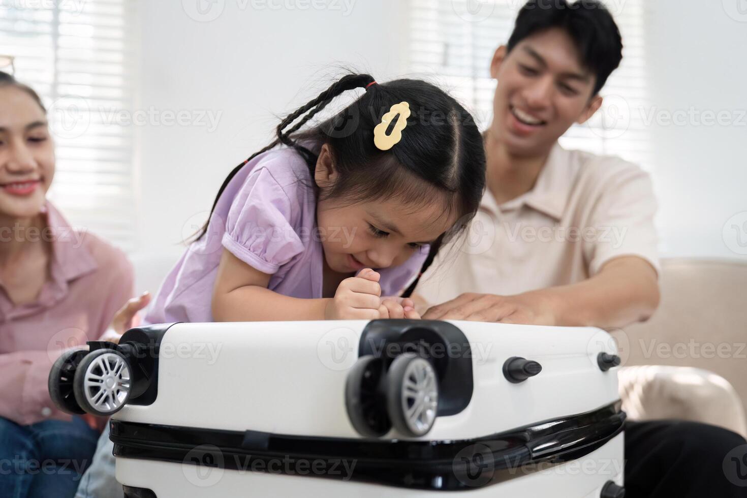 Playful Exploration and Family Fun. A little girl engaged with her suitcase while her parents cheer her on. photo