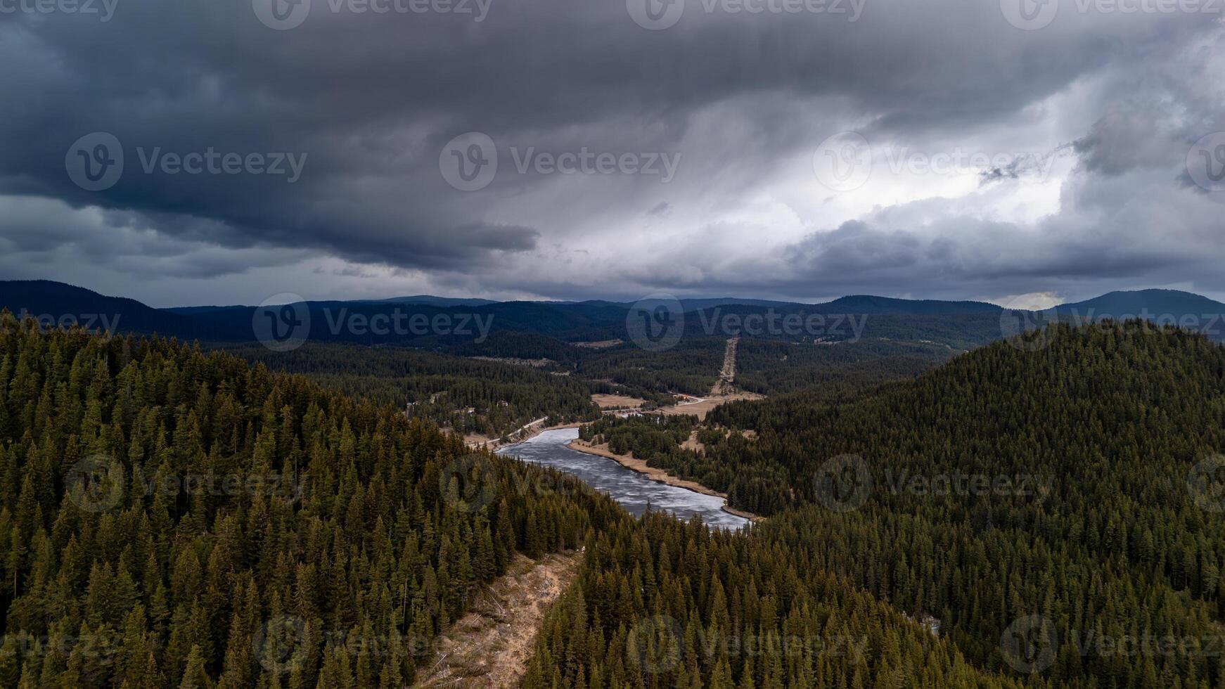 Dramatic sky over pine forest and frozen lake in mountain valley photo