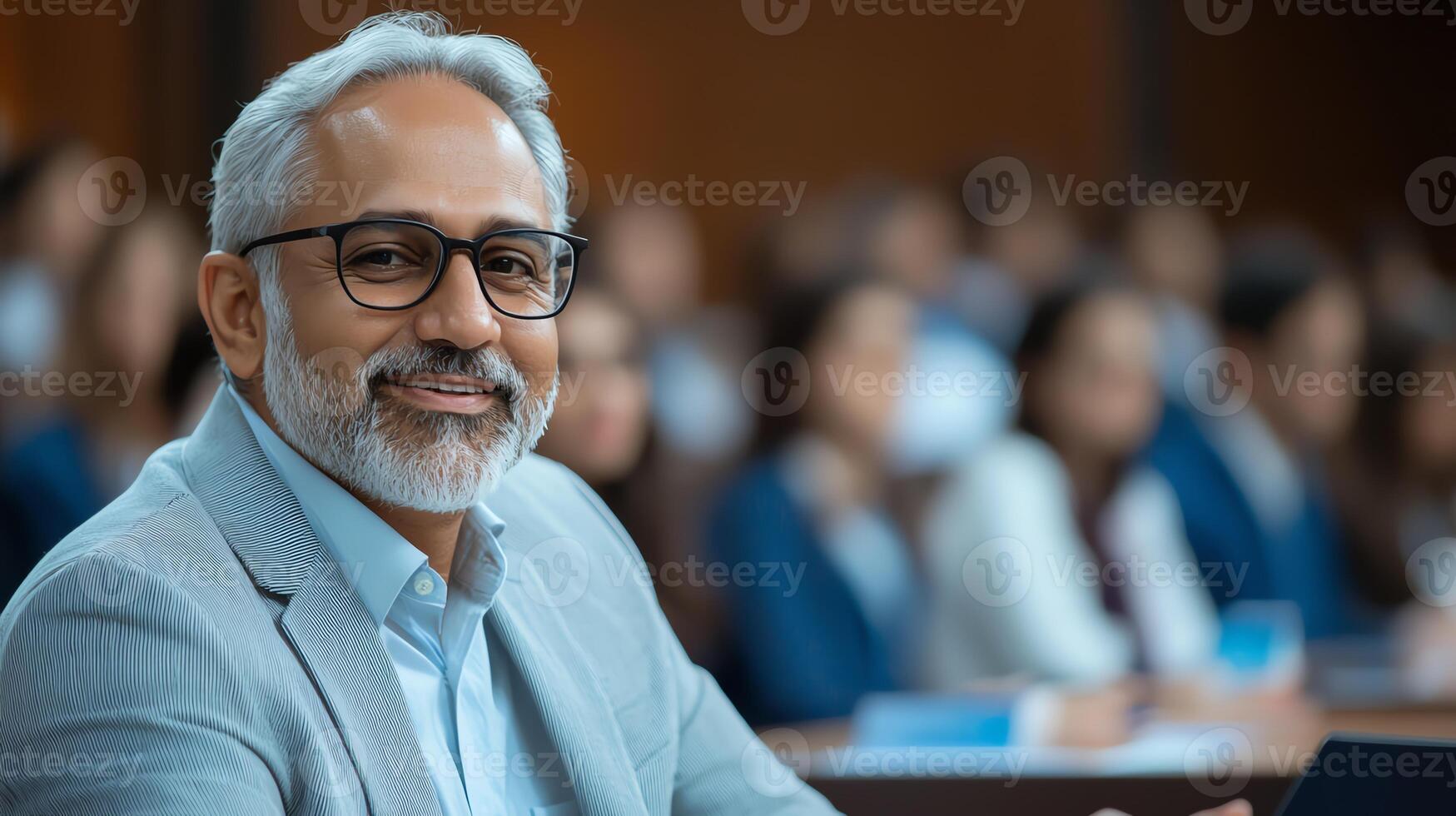 A confident older man in a professional setting, wearing glasses and a suit, smiling among colleagues in an office environment. photo