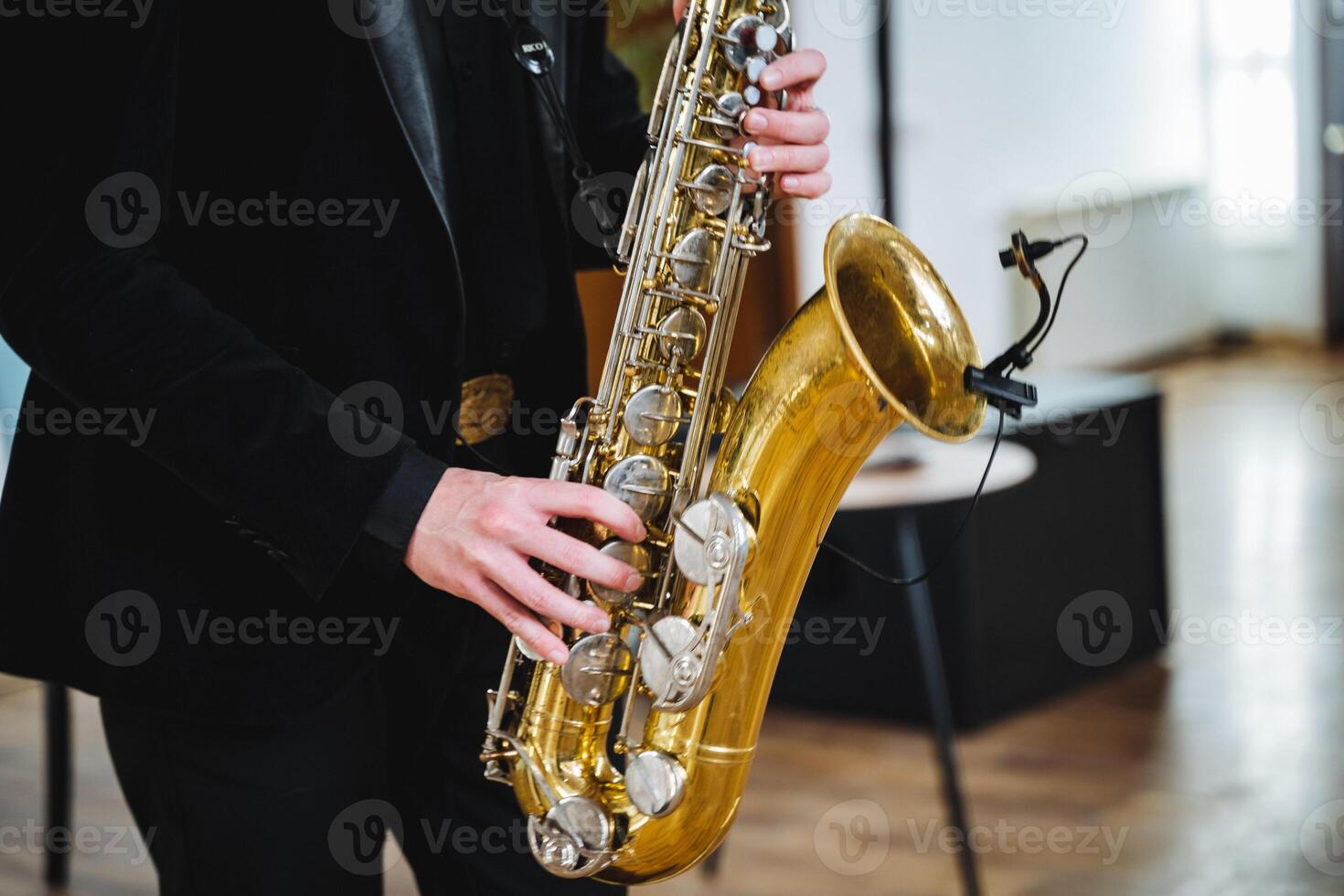 A man dressed in a stylish formal suit skillfully plays a saxophone while standing next to a microphone, producing a captivating melody that beautifully resonates throughout the entire room photo
