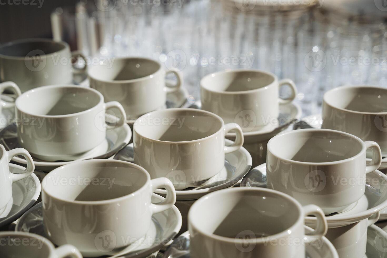 On a table, there is a collection of white coffee cups and their matching saucers, neatly arranged, beckoning for a cozy coffee moment or delightful tea time conversation photo
