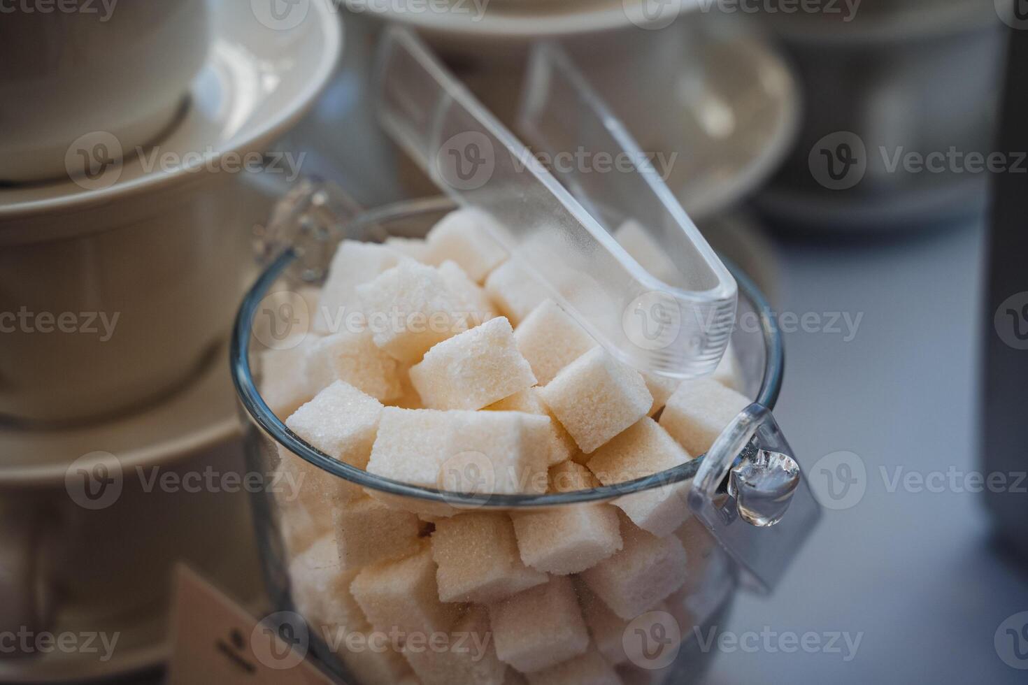A beautifully arranged table features a glass filled to the brim with delightful sugar cubes and a handy scoop, creating an inviting presentation of sweet culinary possibilities photo